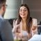 Portrait of joyful  woman smiling and holding resume while sitting in front of businessman during corporate meeting or job interview - business, career and placement concept